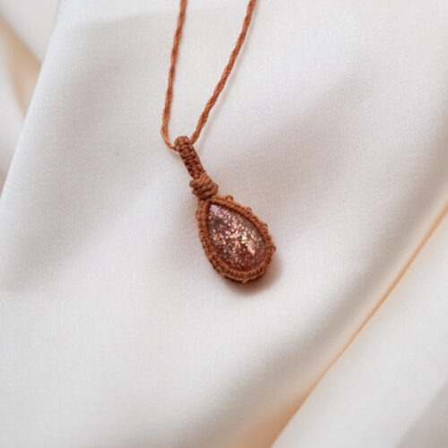 Sonne im Herzen – Makramee Ketten mit Sonnenstein  ☀️🧡 Sonne im Herzen steht für Wärme, Zuversicht und die Erinnerung an das eigene innere Licht. Diese Ketten vereinen sorgfältig ausgewählte Sonnensteine, die in feiner Makramee-Arbeit gefasst sind. Jeder Knoten hält den Stein achtsam und macht jede Kette zu einem Einzelstück. Der Sonnenstein wird traditionell mit Lebensfreude, Optimismus und innerer Stärke verbunden. Er unterstützt dabei, Vertrauen in sich selbst zu entwickeln, den eigenen Wert zu erkennen und dem Leben mit mehr Offenheit zu begegnen. Seine warme Ausstrahlung erinnert daran, dass Licht auch in stillen Momenten präsent sein darf. Die Makramee-Fassung unterstreicht diese Qualität. Sie hält den Stein nicht fest, sondern trägt ihn – flexibel, organisch und lebendig. Sonne im Herzen ist eine Kollektion für Menschen, die sich nach Wärme, Aufrichtung und einer leisen, stabilen Zuversicht sehnen. ✨ Themen: Mental: Optimismus, Lebensfreude, Urvertrauen, Selbstvertrauen, innerer Wachstum, Inspiration, Achtsamkeit, Annahme, innere Stärke Chakra: Sakralchakra Element: Feuer Sternzeichen: Löwe, Waage, Jungfrau, Widder 🗿 Mineralogische & historische Fakten: Der Sonnenstein gehört zur Feldspatgruppe und zeigt einen typischen goldrötlichen Glanz (Aventureszenz), der durch Einschlüsse wie Hämatit oder Goethit entsteht. Chemisch handelt es sich meist um einen Oligoklas oder Labradorit. Bereits in der Antike wurde er als Stein des Lichtes und der Götter verehrt. Die Wikinger nutzten vermutlich transparente Varianten als Navigationshilfe – um auch bei bedecktem Himmel die Sonne zu orten. In der spirituellen Arbeit steht der Sonnenstein für Freude, Leichtigkeit und das innere Strahlen. Er erinnert daran, dass selbst hinter dunklen Wolken immer die Sonne scheint.