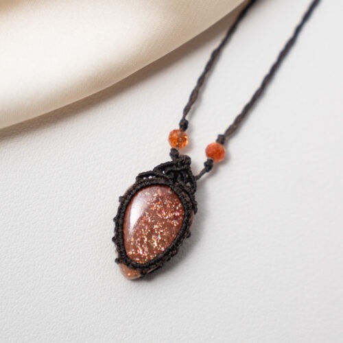 Sonne im Herzen – Makramee Ketten mit Sonnenstein  ☀️🧡 Sonne im Herzen steht für Wärme, Zuversicht und die Erinnerung an das eigene innere Licht. Diese Ketten vereinen sorgfältig ausgewählte Sonnensteine, die in feiner Makramee-Arbeit gefasst sind. Jeder Knoten hält den Stein achtsam und macht jede Kette zu einem Einzelstück. Der Sonnenstein wird traditionell mit Lebensfreude, Optimismus und innerer Stärke verbunden. Er unterstützt dabei, Vertrauen in sich selbst zu entwickeln, den eigenen Wert zu erkennen und dem Leben mit mehr Offenheit zu begegnen. Seine warme Ausstrahlung erinnert daran, dass Licht auch in stillen Momenten präsent sein darf. Die Makramee-Fassung unterstreicht diese Qualität. Sie hält den Stein nicht fest, sondern trägt ihn – flexibel, organisch und lebendig. Sonne im Herzen ist eine Kollektion für Menschen, die sich nach Wärme, Aufrichtung und einer leisen, stabilen Zuversicht sehnen. ✨ Themen: Mental: Optimismus, Lebensfreude, Urvertrauen, Selbstvertrauen, innerer Wachstum, Inspiration, Achtsamkeit, Annahme, innere Stärke Chakra: Sakralchakra Element: Feuer Sternzeichen: Löwe, Waage, Jungfrau, Widder 🗿 Mineralogische & historische Fakten: Der Sonnenstein gehört zur Feldspatgruppe und zeigt einen typischen goldrötlichen Glanz (Aventureszenz), der durch Einschlüsse wie Hämatit oder Goethit entsteht. Chemisch handelt es sich meist um einen Oligoklas oder Labradorit. Bereits in der Antike wurde er als Stein des Lichtes und der Götter verehrt. Die Wikinger nutzten vermutlich transparente Varianten als Navigationshilfe – um auch bei bedecktem Himmel die Sonne zu orten. In der spirituellen Arbeit steht der Sonnenstein für Freude, Leichtigkeit und das innere Strahlen. Er erinnert daran, dass selbst hinter dunklen Wolken immer die Sonne scheint.